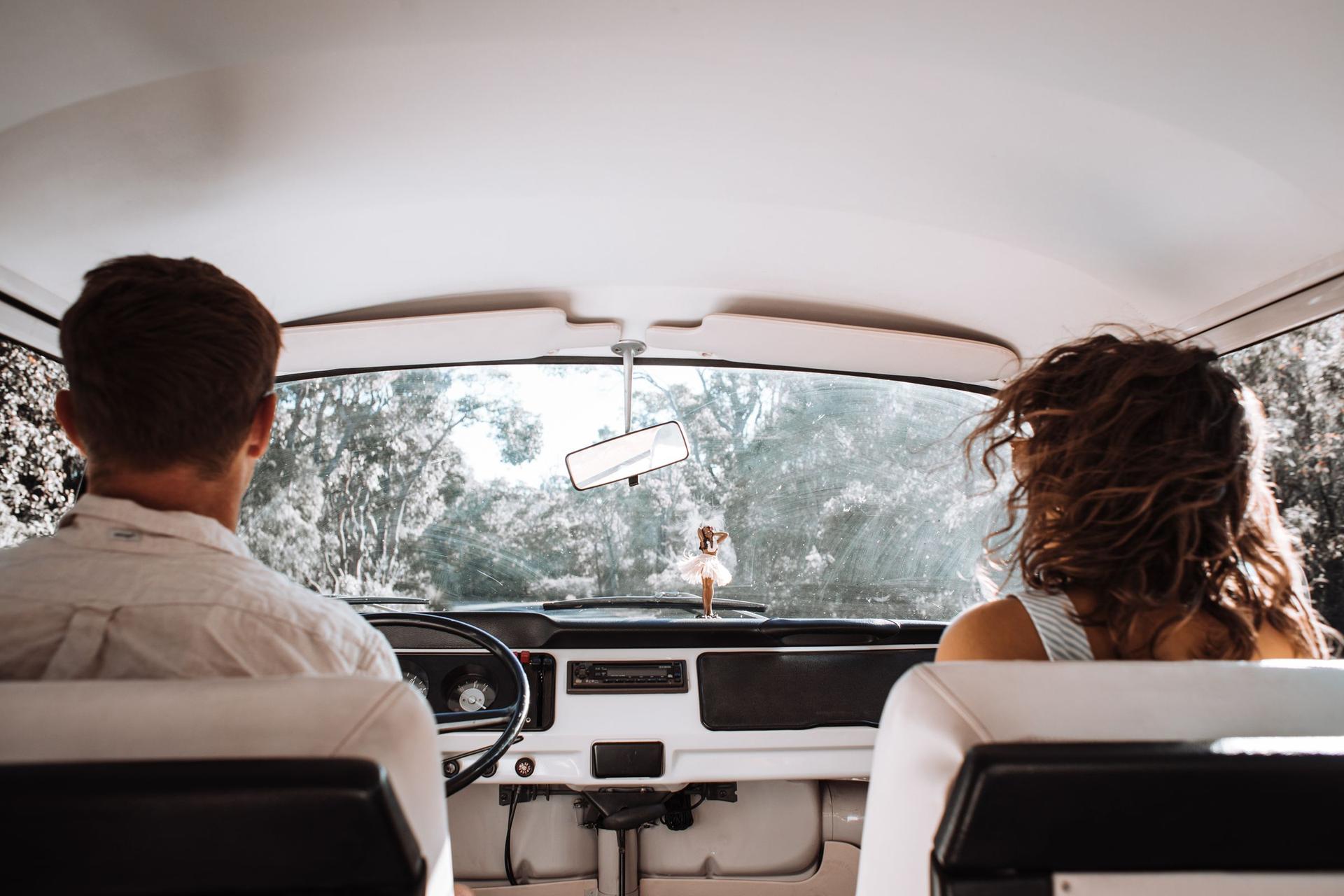 Couple driving a classic car on a sunny tree-lined road, covered by auto insurance
