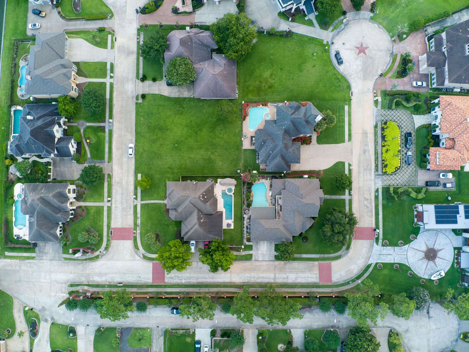 Aerial view of a suburban neighborhood with homes, pools, and tree-lined streets