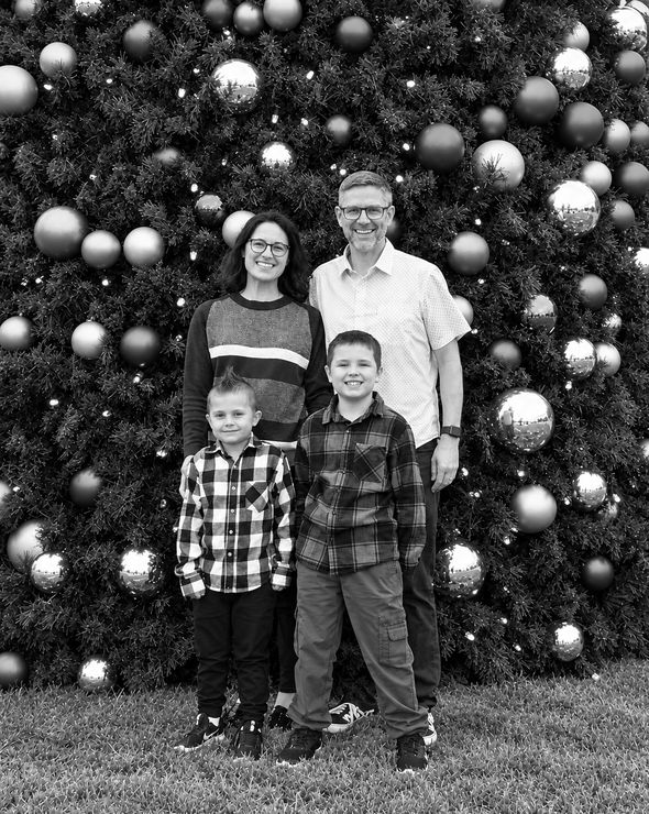 Black and white photo of Lance Thomas with his wife and two young sons, standing in front of a large Christmas tree decorated with ornaments