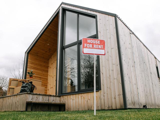 Modern wood-sided house with a red House for Rent sign on the front lawn, representing landlord insurance