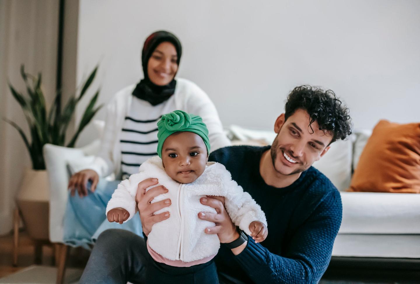 Smiling parents playing with their baby daughter on the living room floor, representing life insurance