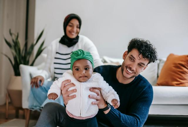 Smiling parents playing with their baby daughter on the living room floor, representing life insurance