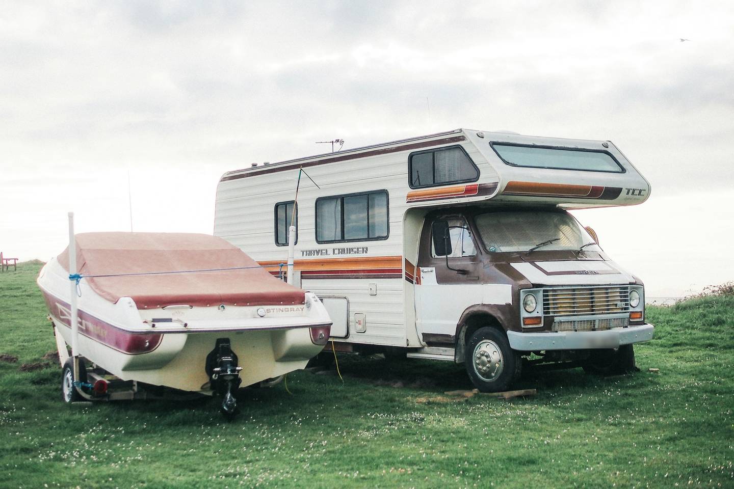 Vintage Class C motorhome parked on a grassy field beside a covered speedboat on its trailer